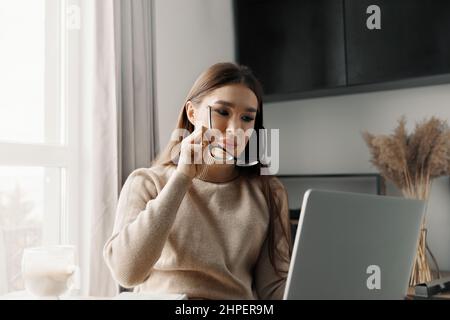 Schöne glückliche Frau, die zu Hause mit Laptop arbeitet. Lächelnde Geschäftsfrau, die im Büro am Computer eine Brille trägt Stockfoto