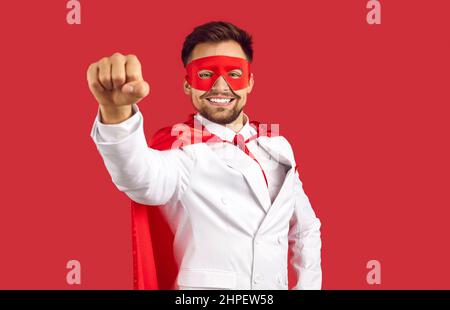 Porträt eines selbstbewussten jungen Mannes in Superhelden-Maske und Umhang, der seine Hand ausstreut und lächelt Stockfoto