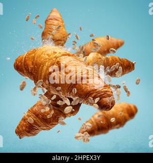 Frisch gebackene Croissants fliegen in der Luft auf blauem Hintergrund Stockfoto