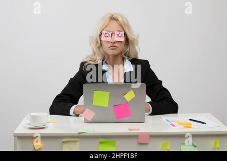 Viel Arbeit Konzept. Müde junge Geschäftsfrau, die mit Aufklebern auf den Augen geschlafen hat und am Arbeitsplatz sitzt Stockfoto