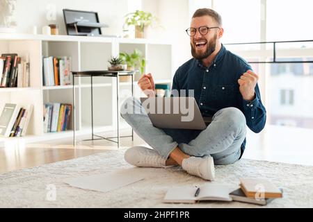 Emotionaler Freiberufler, Der Mit Dem Laptop Schreit, Um Den Erfolg Zu Hause Zu Feiern Stockfoto