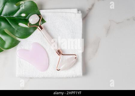 Gesichtswalzen, Massagegerät guasha Scraper, aus natürlichem Quarzstein. Self-Care-Set. Hausgemachte Spa-Produkte auf einem Wtite Handtuch auf Marmor Hintergrund, die c Stockfoto