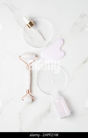 Rosa flüssiges Gel oder Hyaluronserum in Petrischale mit Pipette. Gua Sha Set Werkzeuge zum Massieren. Feuchtigkeitsspendende und hautpflegende Konzept. Stockfoto