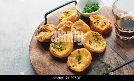 Leckere Eiermuffins mit grünen Zwiebeln, Speck, Käse und Tomaten auf Holzbrett auf hellem Hintergrund. Gesundes, proteinreiches und kohlenhydratarmes Frühstück. Stockfoto