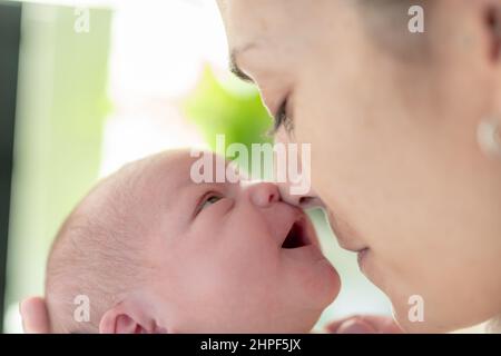 Neugeborenes Baby, das lacht und seinen Mund öffnet, wenn seine Mutter ihre Nase nahe an seine legt. Konzept Pflege, Zuneigung und Schutz des neugeborenen Babys Stockfoto