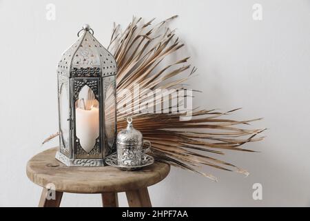 Ramadan Stillleben. Marokkanische silberne, arabische Laterne und eine Tasse türkischer Tee, Kaffee. Braune Palmblätter auf altem Holzhocker. Unscharfer Hintergrund Stockfoto