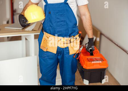 Ausgeschnittene Aufnahme eines Bauarbeiters in Overalls und Hardhut mit Werkzeugkasten, der drinnen steht Stockfoto