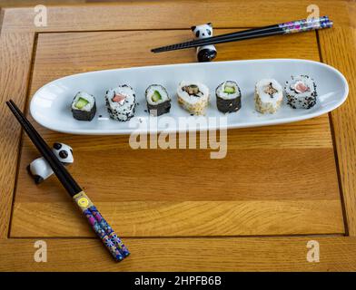 Frisches Sushi auf einer weißen Servierplatte mit zwei Paar Essstäbchen, die auf Pandahaltern ruhen Stockfoto