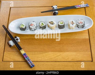 Frisches Sushi auf einer weißen Servierplatte mit zwei Paar Essstäbchen, die auf Pandahaltern ruhen Stockfoto