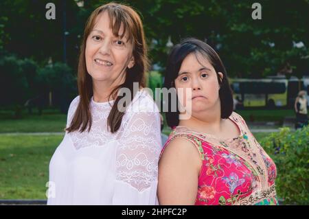 Porträt der kaukasischen lateinischen Mutter und Tochter zusammen auf einem Platz Blick auf die Kamera, Inklusion, Menschen mit Behinderungen und Lifestyle-Konzept. Stockfoto