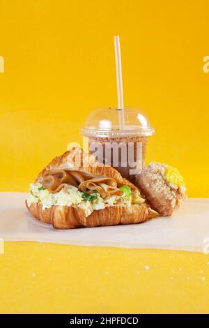 Brioched Criossant Rührei Sandwich mit kaltem Kaffee und Donut. Stockfoto