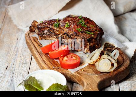 Nahaufnahme-Steak mit T-Knochen. Appetitlich gegrilltes Fleisch mit Gemüse und Kräutern Stockfoto