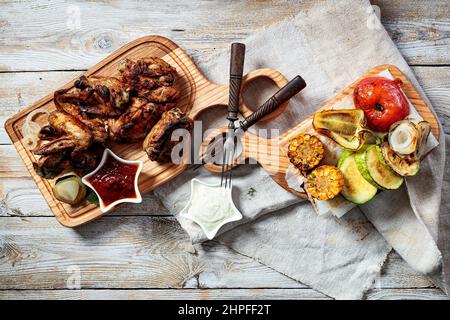 Heißer Grill Hähnchenflügel auf einem Schneidebrett und verschiedene Grillgemüse. Appetitlich gegrilltes Hähnchenfleisch mit Gemüse und Kräutern, Sauce. Obere V Stockfoto