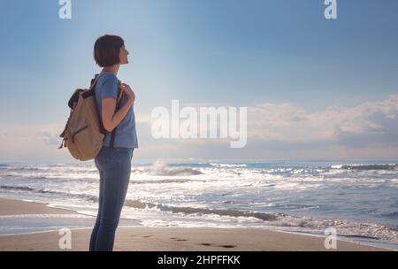 Backpacker-Weibchen sitzen am Strand der Sanddünen von Patara und genießen das windige Mittelmeer während des Lykischen Wanderwegs. Berühmte Likya Yolu türkische Route. Image des Urlaubskonzepts für aktive Menschen Stockfoto