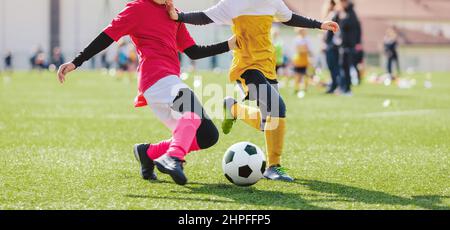Schulmädchen und -Jungen spielen Fußballspiel. Kinder haben Spaß und spielen Fußballspiel. Mädchen in rosa Fußballuniform tritt Ball Stockfoto