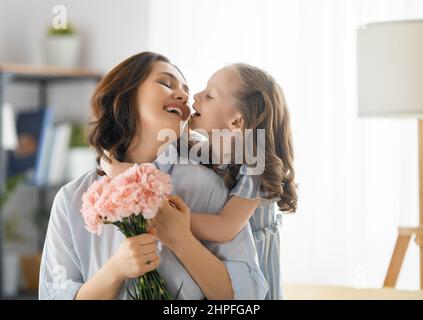 Guten Tag! Die Tochter gratuliert der Mutter und schenkt ihr Blumen. Mama und Mädchen lächeln und umarmen. Familienurlaub und Zweisamkeit. Stockfoto