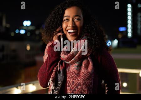 Porträt einer selbstbewussten jungen erwachsenen Biracial-Frau, die auf der Dachterrasse bei einer Party auf dem Handy spricht. Stockfoto