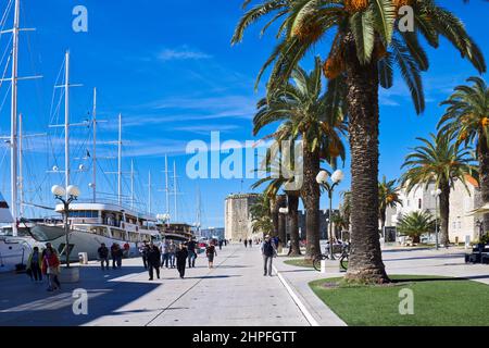 Altstadt von Trogir, Kroatien - Menschen, die an einem sonnigen Tag entlang der Riva oder der Promenade neben festverankerten Yachten spazieren Stockfoto