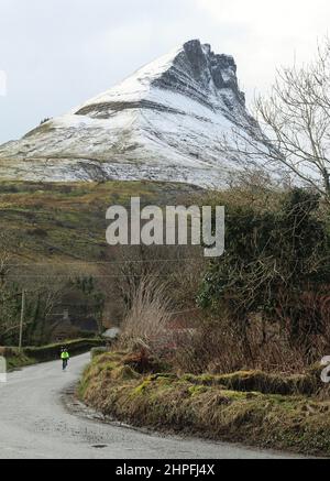 Radfahrer unterwegs am Fuß des schneebedeckten Benwiskin-Berges im Winter, Ballintrillick, County Sligo, Irland Stockfoto