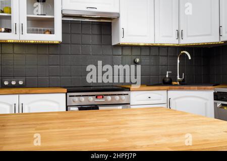 Moderne weiße Wohnküche mit massiver, naturfarbener Eichenholzplatte und verschiedenen Geräten. Stockfoto