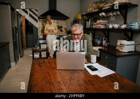 Lächelnder älterer Mann, der am Küchentisch sitzt Stockfoto
