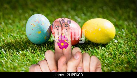 Nahaufnahme von beschnittenen Händen mit Hasen, die auf Zeigefingern gegen ostereier auf Gras ziehen Stockfoto