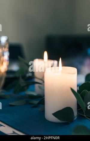 Nahaufnahme, brennende Kerzen auf dem Tisch zwischen den Blättern. Stockfoto