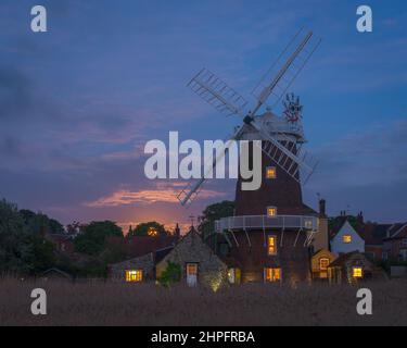 Ein Vollmond, der durch die dicken Wolken hinter der Windmühle bei Cley am Meer aufsteigt, entlang des Flusses Glaven an der Norfolk-Küste, England, Großbritannien Stockfoto