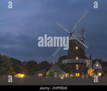 Ein Vollmond, der durch die dicken Wolken hinter der Windmühle bei Cley am Meer aufsteigt, entlang des Flusses Glaven an der Norfolk-Küste, England, Großbritannien Stockfoto