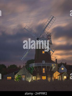 Ein Vollmond, der durch die dicken Wolken hinter der Windmühle bei Cley am Meer aufsteigt, entlang des Flusses Glaven an der Norfolk-Küste, England, Großbritannien Stockfoto