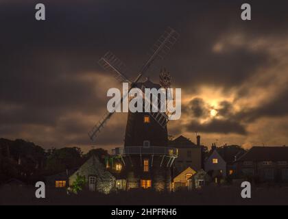 Ein Vollmond, der durch die dicken Wolken hinter der Windmühle bei Cley am Meer aufsteigt, entlang des Flusses Glaven an der Norfolk-Küste, England, Großbritannien Stockfoto