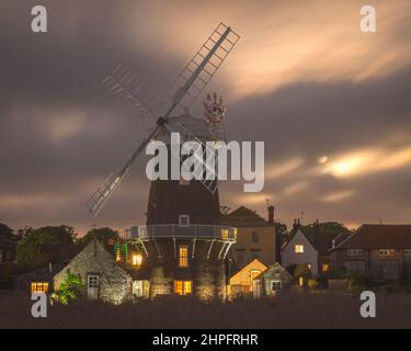 Ein Vollmond, der durch die dicken Wolken hinter der Windmühle bei Cley am Meer aufsteigt, entlang des Flusses Glaven an der Norfolk-Küste, England, Großbritannien Stockfoto