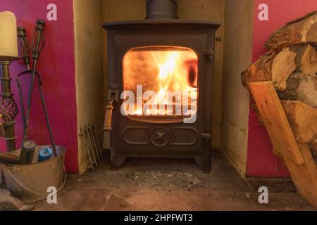 Gusseisen, Holzofen, Glastür, auf Schieferfliesen im offenen Kamin, brennend. Stockfoto
