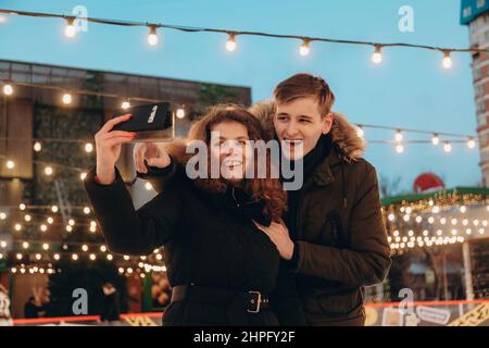 Ein junges verliebtes Paar umarmt sich und macht ein Selfie auf einer Eisbahn. Stockfoto