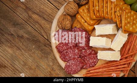 Fleisch- und Käseplatte für Vorspeisen. Wurst, Käse, Cracker, Nüsse auf Holzplatte und Hintergrund. Draufsicht, für Text platzieren. Stockfoto