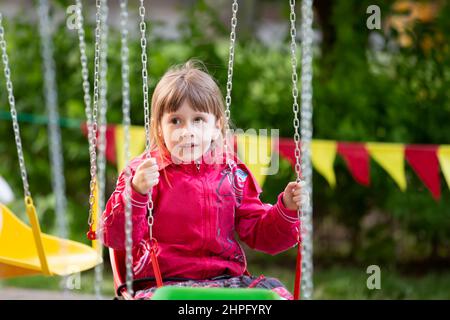 Ein kleines Mädchen in einer roten Jacke sitzt auf einer Karussellfahrt. Stockfoto