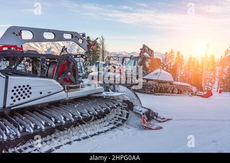 Parken auf einer Piste Schneeräumgeräte für ein Skigebiet. Schneepflügen Bulldozer Grooming für Ski- und Snowboardferien am Berg bei Sonnenuntergang Stockfoto