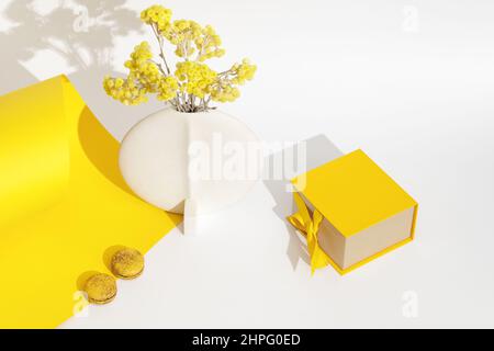 Immerwährende immortelle gelbe Blüten in minimalistischer weißer Keramikvase, zwei französischen Makronen und einer gelben Geschenkbox mit Schleife über Gelb und Whi Stockfoto