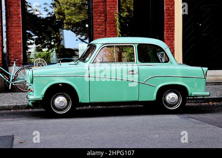 Grün - türkisfarbener trabant, umgebaut als Cadillac-Auto und türkisfarbenes Fahrrad, das vor einem Geschäft steht Stockfoto