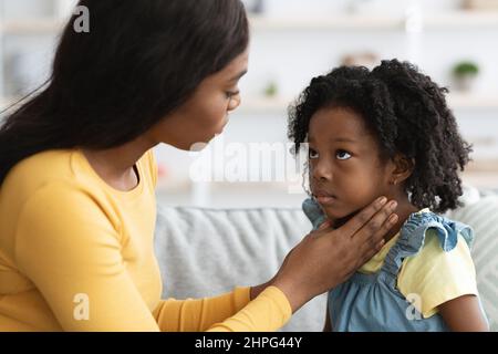 Schwarze Mutter kümmert sich um ihr krankes Kind, das an Halsschmerzen leidet Stockfoto