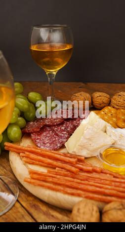 Snacks für Wein. Käse- und Fleischplatte. Wurst, Käse, Nüsse, Trauben, Cracker auf Holzgrund. Vertikales Foto Stockfoto