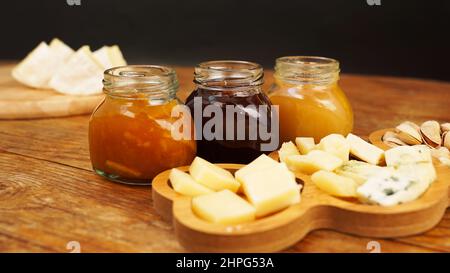 Gläser mit hausgemachten Marmeladen und Honig in Gläsern und einer Vielzahl von Käsesorten auf einem Holztisch. Käseplatte für Vorspeisen. Stockfoto