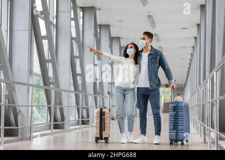 Arabisches Paar In Schutzgesichtsmasken, Das Am Flughafen Steht Und Zur Seite Zeigt Stockfoto