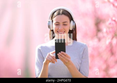 Vorderansicht Porträt einer glücklichen Frau, die durch ein Feld läuft und Musik hört Stockfoto