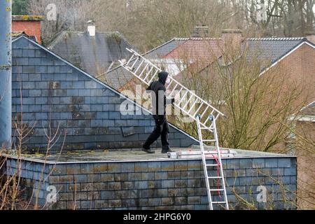 Dachdecker / Dachdecker Installation von Leitern auf dem Dach für Reparaturarbeiten an einem stürmischen Tag nach Durchgang der Stürme Eunice und Franklin im Februar 2022 Stockfoto