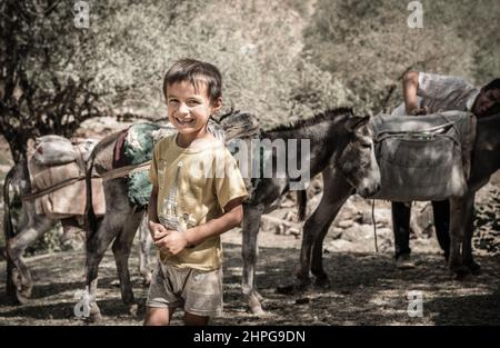 25. August 2016, Shirkent Valley, Tadschikistan: Der einheimische Junge posiert für die Kamera, während sein Vater Maultiere im Hintergrund einpacken will Stockfoto