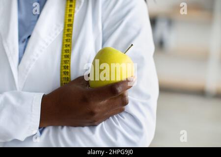 Ein Apfel am Tag und ein Virus weg. Grüner frischer Apfel in schwarzer ärztlicher Hand, Ernährungsberaterin posiert mit Maßband Stockfoto