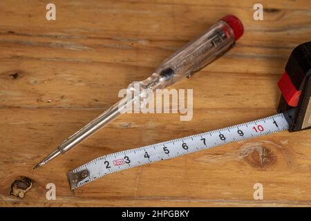 Auf einem Holztisch liegen alte elektrische Spannungsprüfer und weißes Messband, Werkzeuge für Heimwerker Stockfoto