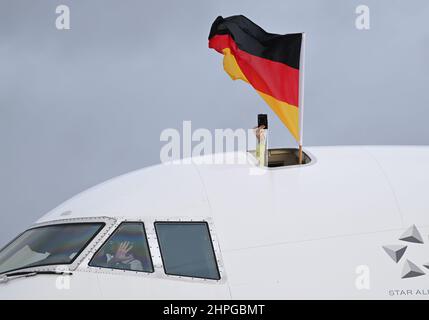 21. Februar 2022, Hessen, Frankfurt/Main: Eine deutsche Flagge und eine Kamera werden aus einer Luke der Lufthansa Boeing 747-800 gehalten, als das deutsche Team von den Olympischen Spielen in Peking am Frankfurter Flughafen zurückkehrt. Foto: Arne Dedert/dpa Stockfoto