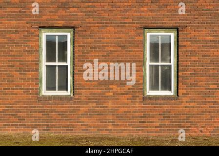 Rote Backsteinmauer mit zwei Fenstern. Stockfoto